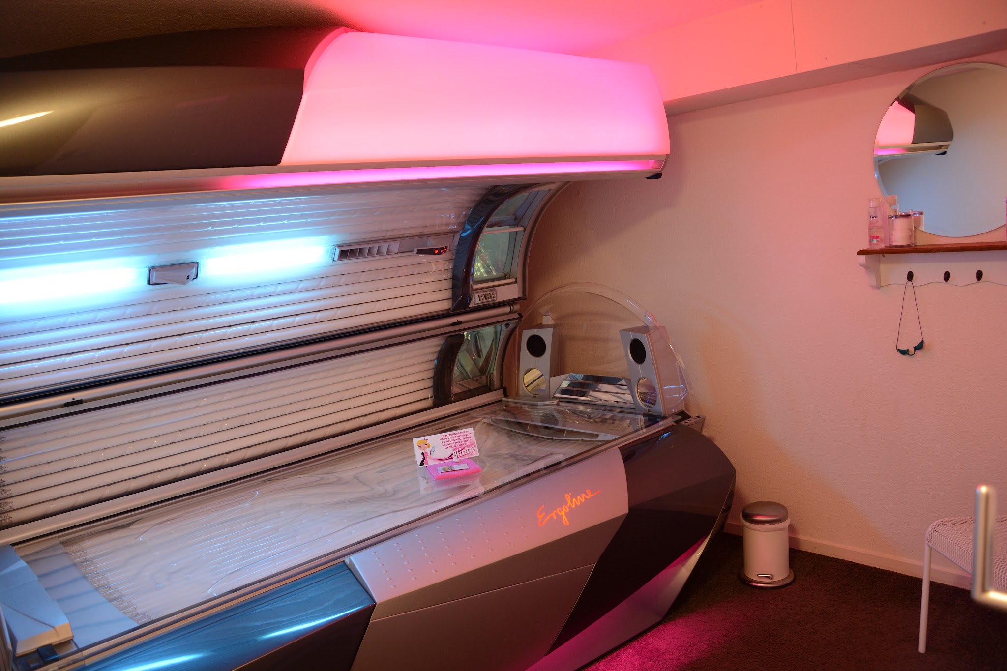 Een geopende Ergoline zonnebank in een cabine van E&V Zonnestudio Horst, verlicht in magenta en cyaan