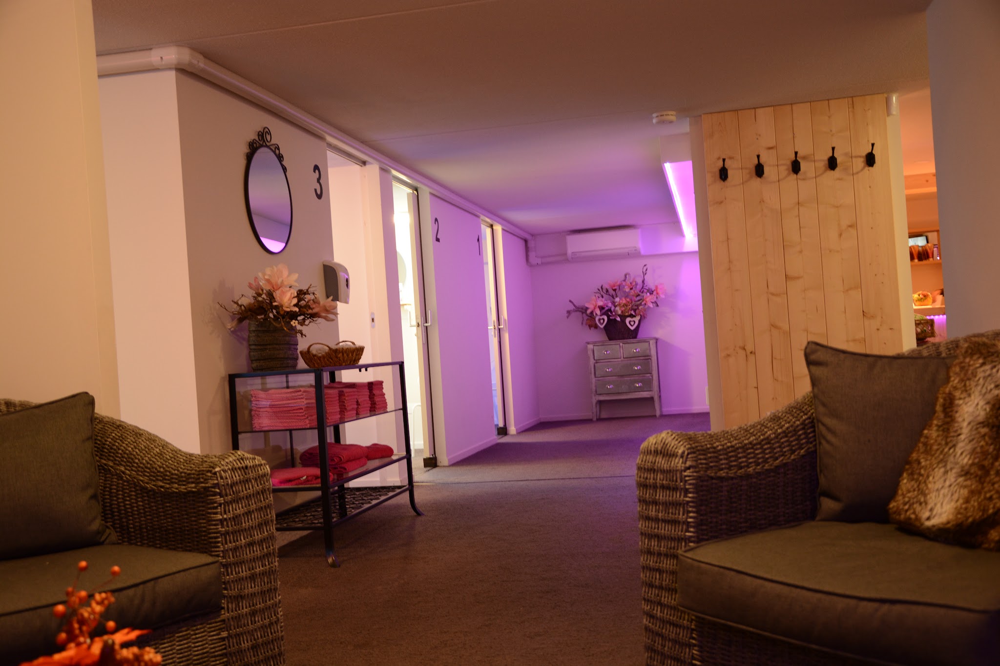 De wachtruimte van de zonnestudio met rieten stoelen, een stapel roze handdoeken en de genummerde cabinedeuren